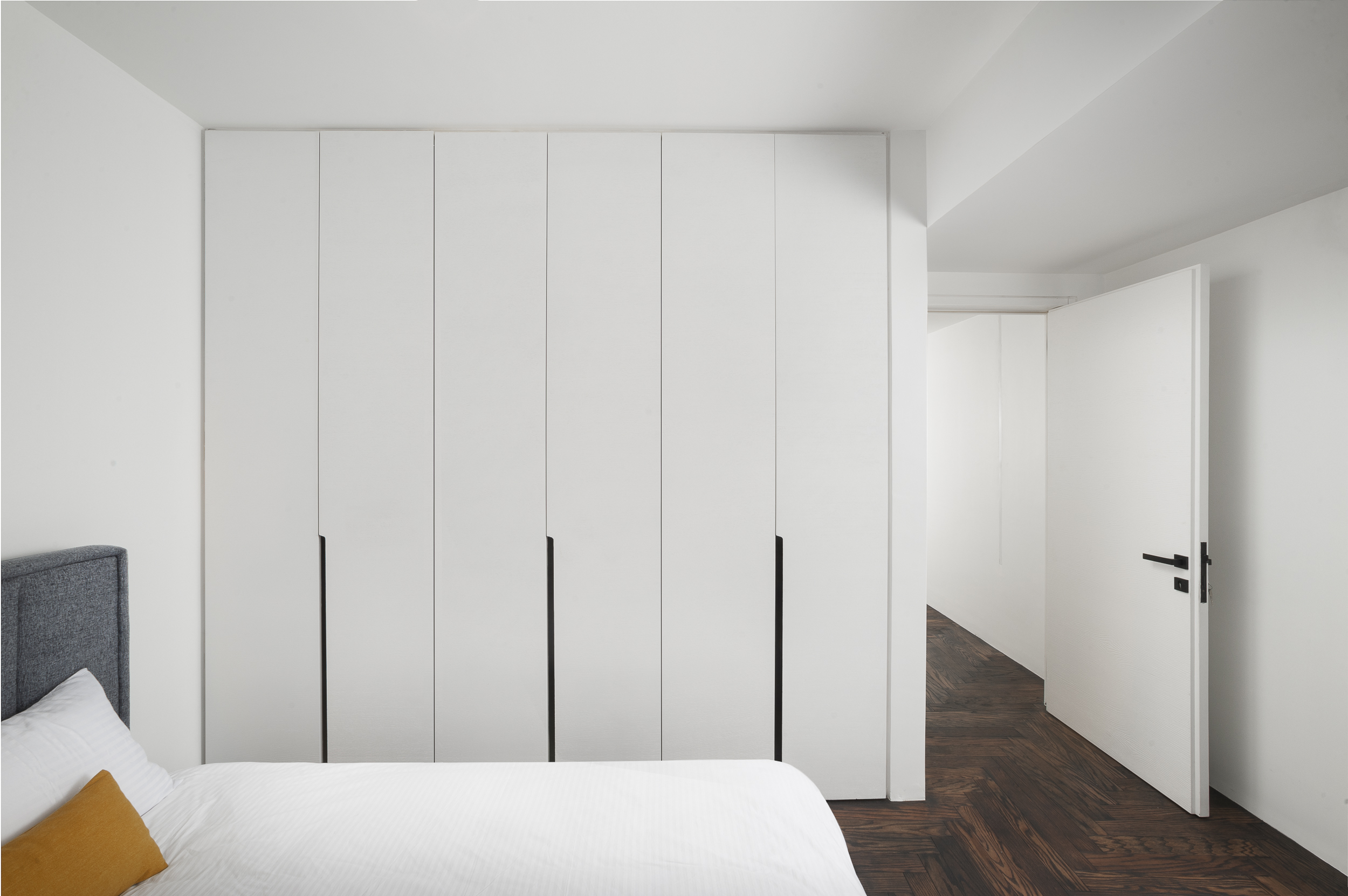 کمد دیواری‌های اتاق خواب به صورت کاملاً یکدست و بدون شکستگی اجرا شده‌اند تا توهم یک دیوار ساده را ایجاد کنند. دستگیره‌های خطی عمودی مشکی، تنها عنصری هستند که عملکرد کمد را آشکار می‌سازند. این طراحی، خلوص بصری اتاق خواب را حفظ می‌کند.